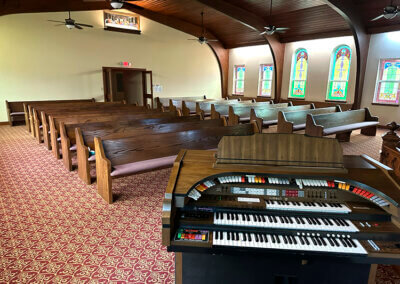 A view of the chapel room from the Organist perspective. The chapel room features a beautiful curved wooden ceiling supported by large beams. The pews are in a beautiful oak wood brown.