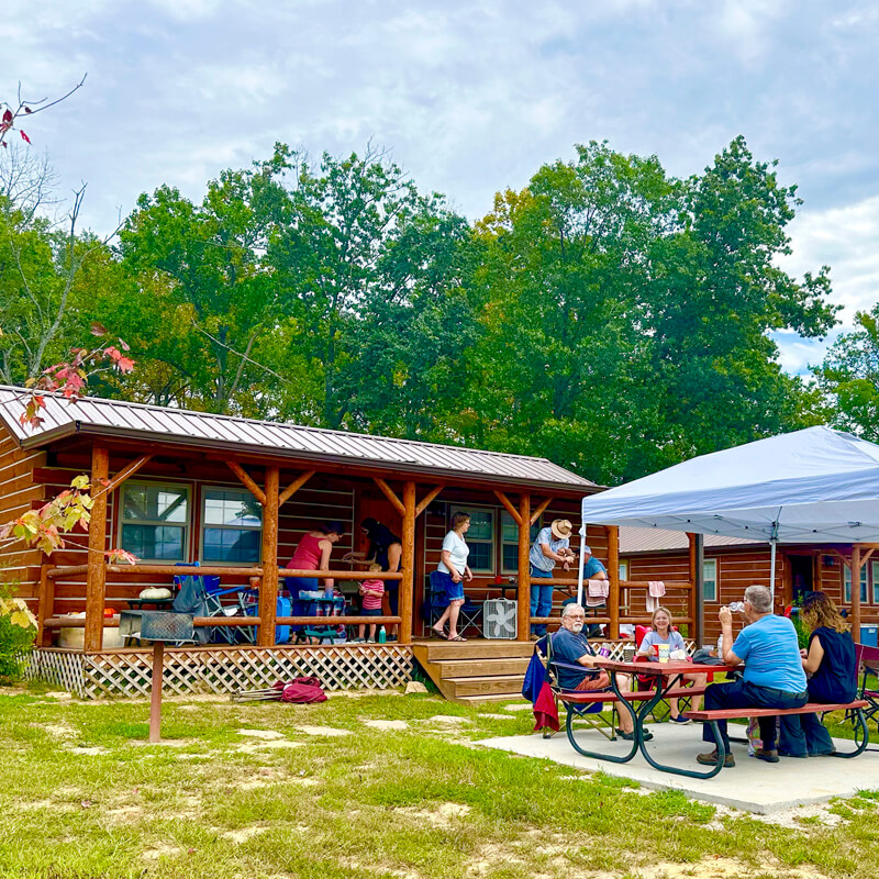 SYCAMORE-SPRINGS-PARK-CAMPING-CABINS-2 A large family group having a cookout in front of one of the camping cabins on an overcast summer day.